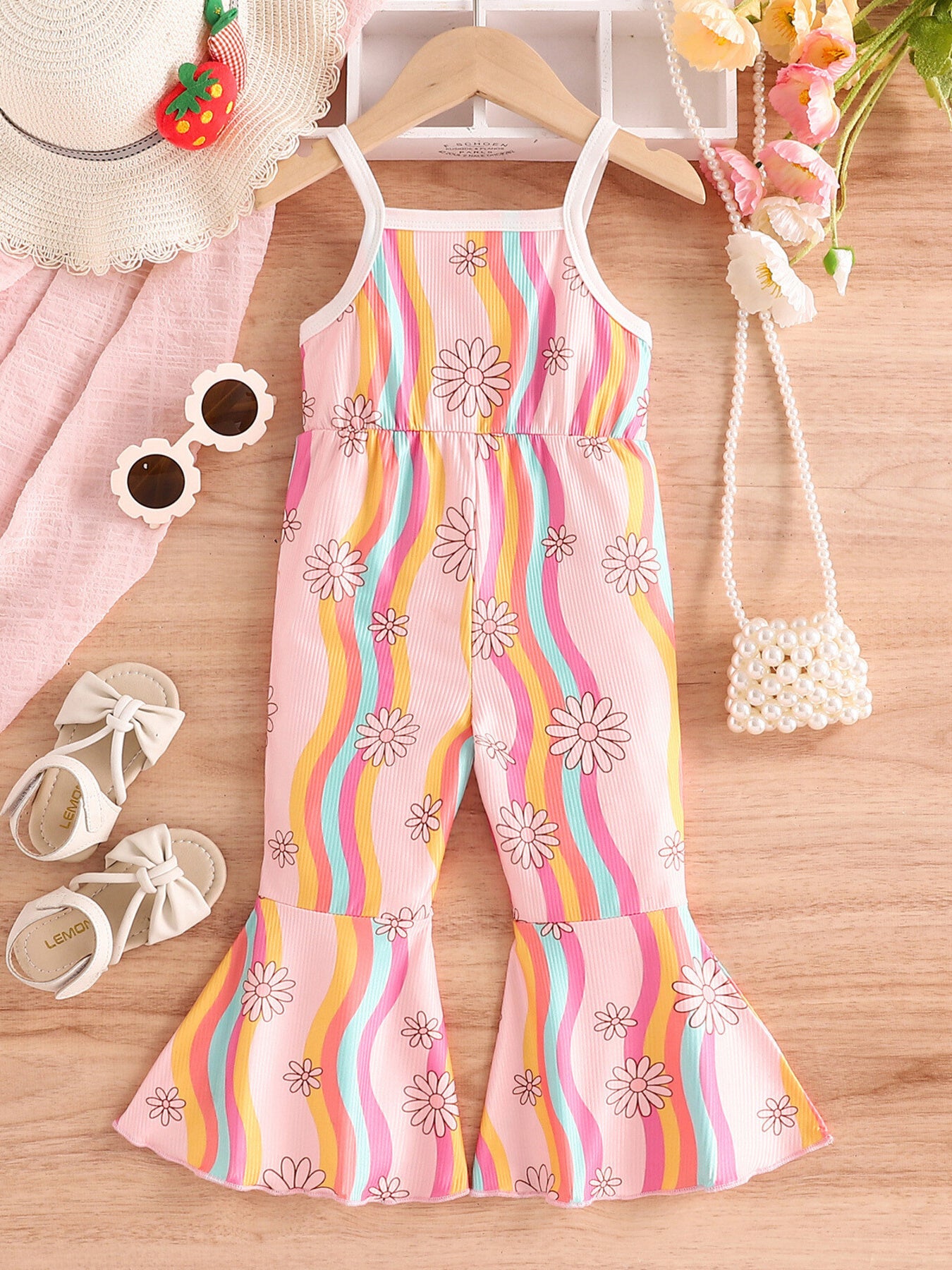 Children's outfit with colorful striped dress on a wooden surface, surrounded by accessories.