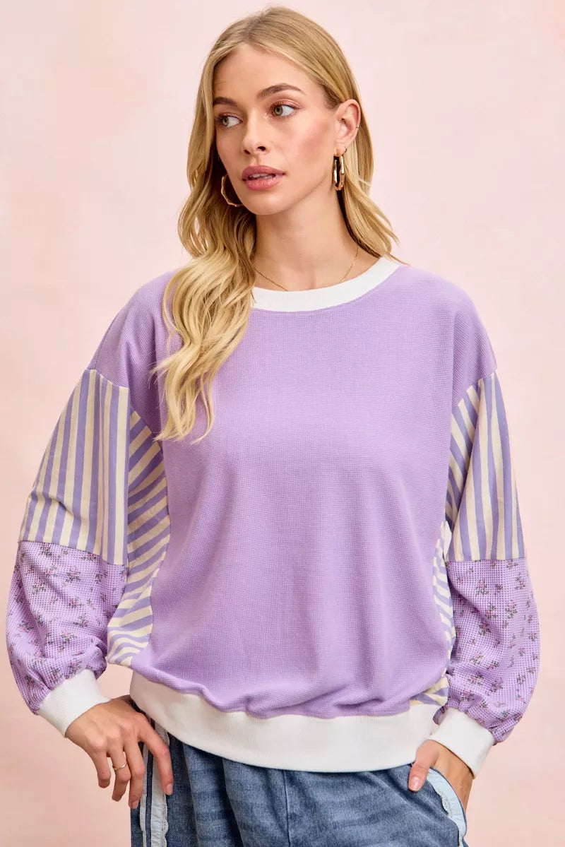 Woman wearing a purple sweater with striped sleeves against a pink background