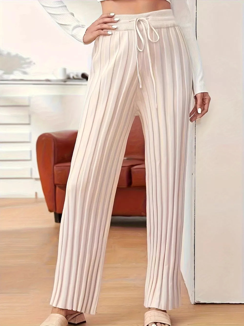 Person wearing white pleated pants in a room with a couch and wooden floor.