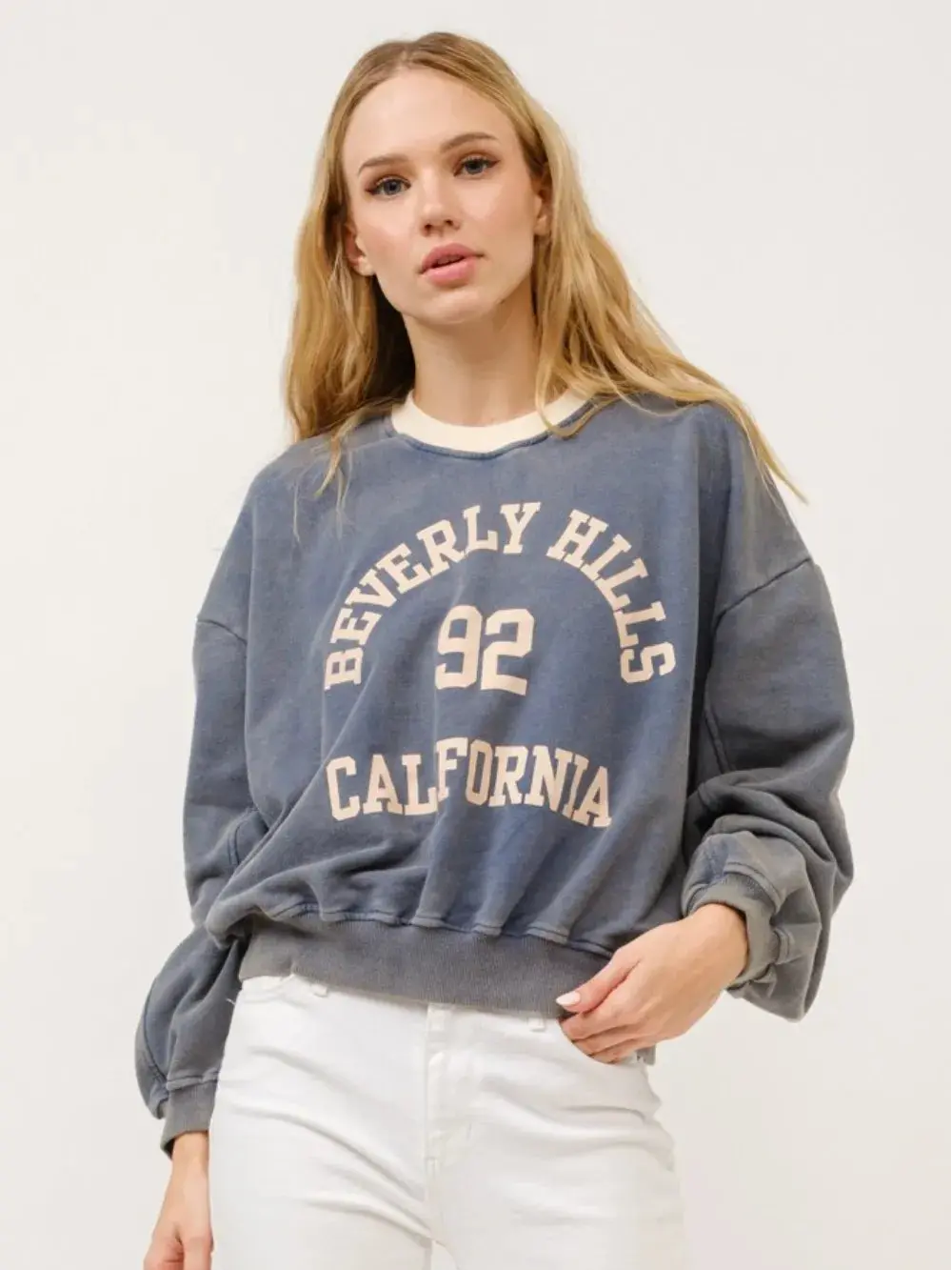 Woman wearing a blue 'Beverly Hills 92 California' sweatshirt against a white background