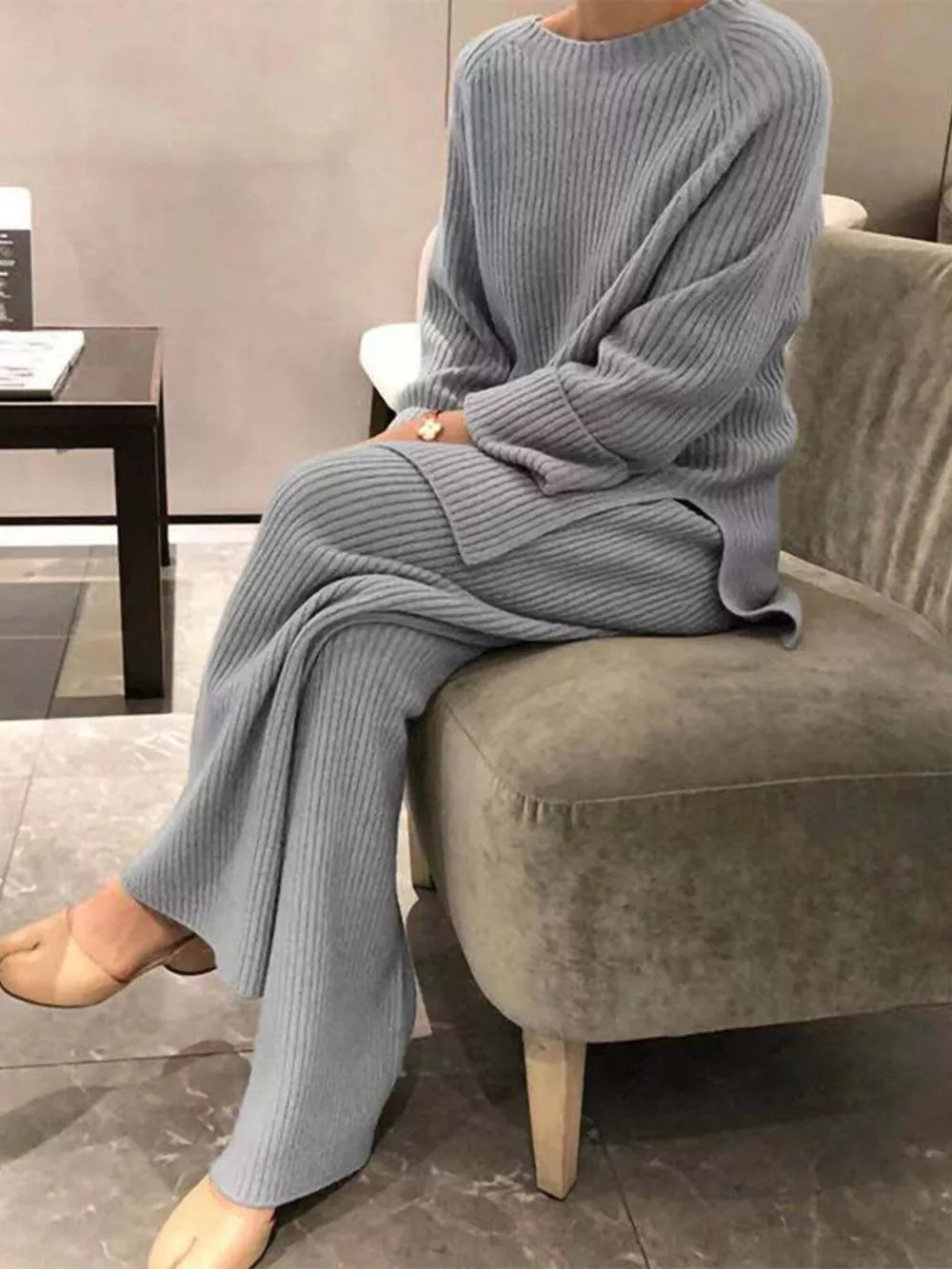 Person wearing a gray knit outfit sitting on a chair in a room.