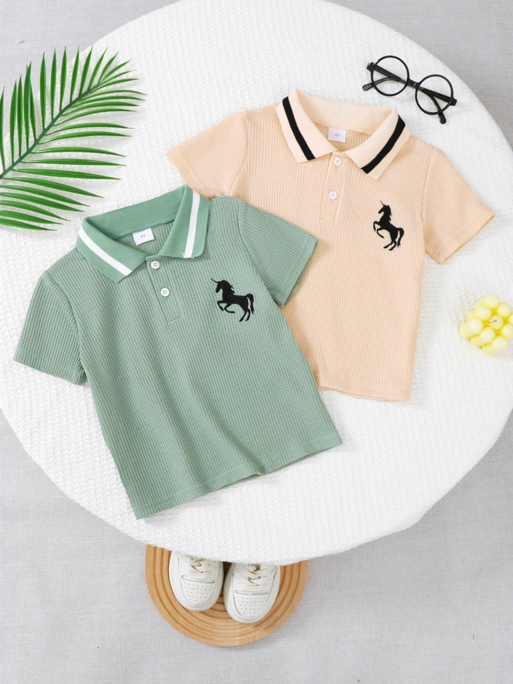 Two polo shirts, one green and one beige, with unicorn designs on a white surface.