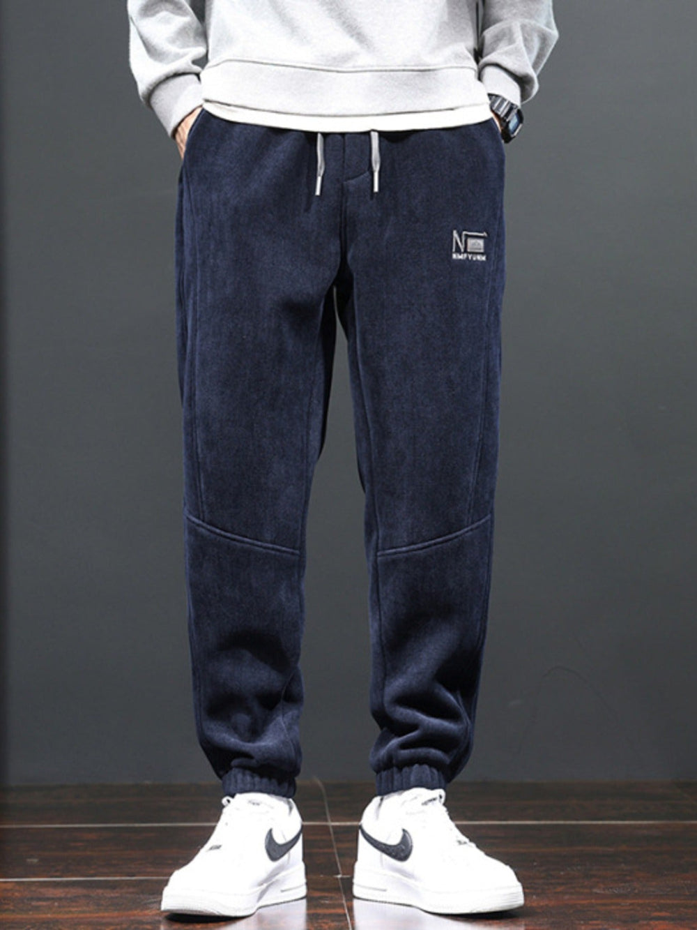 Person wearing navy blue jogger pants with a logo on a gray background